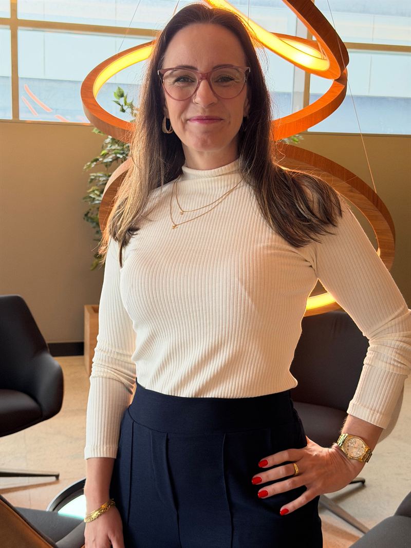 Carla Kerber em pé, com as mãos na cintura, num ambiente corporativo
