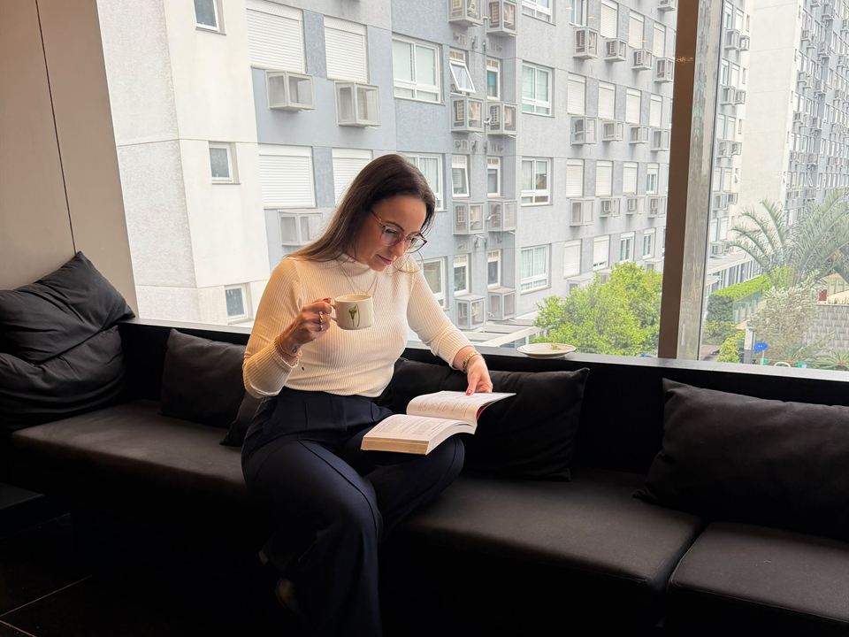 Carla Kerber lendo junto a uma janela ampla com vista para a cidade