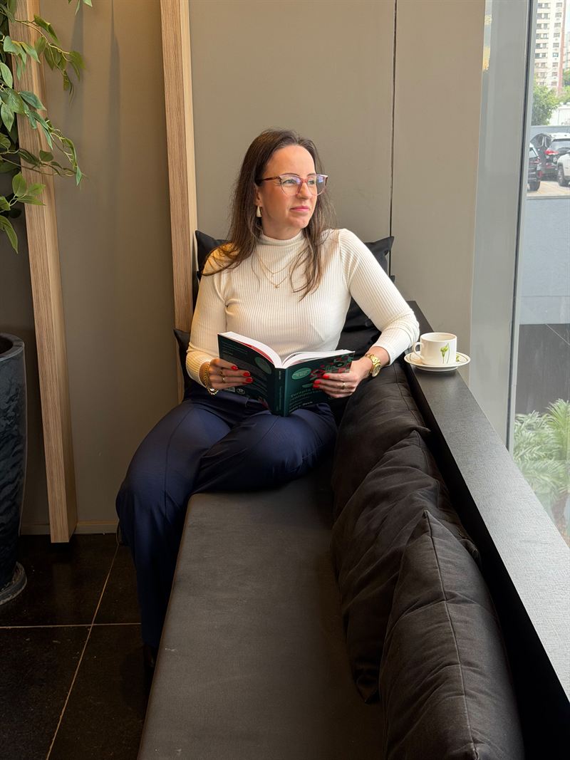 Carla Kerber lendo um livro, sentada junto a uma janela