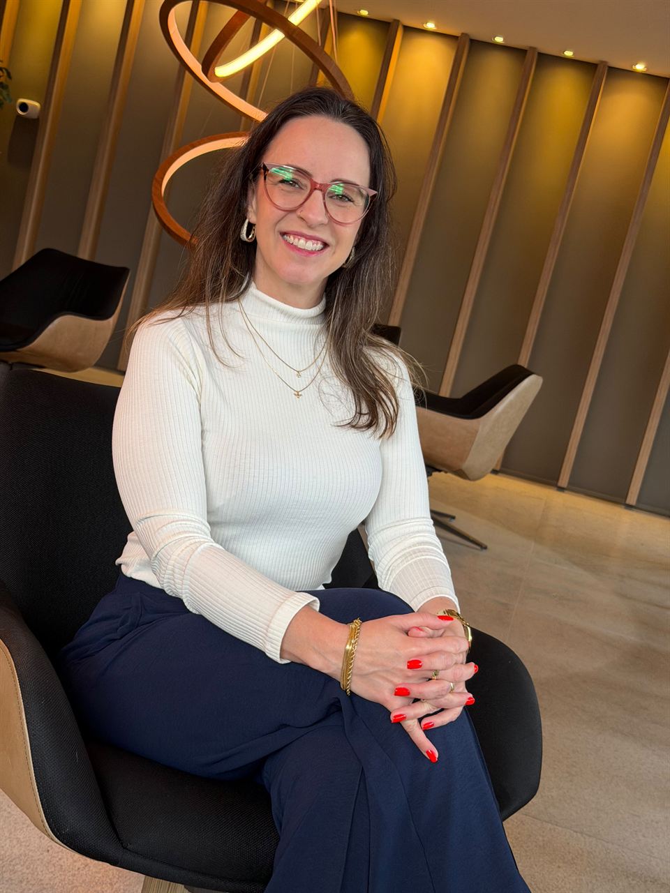 Carla Kerber, psicóloga, sentada numa poltrona, sorrindo para a câmera